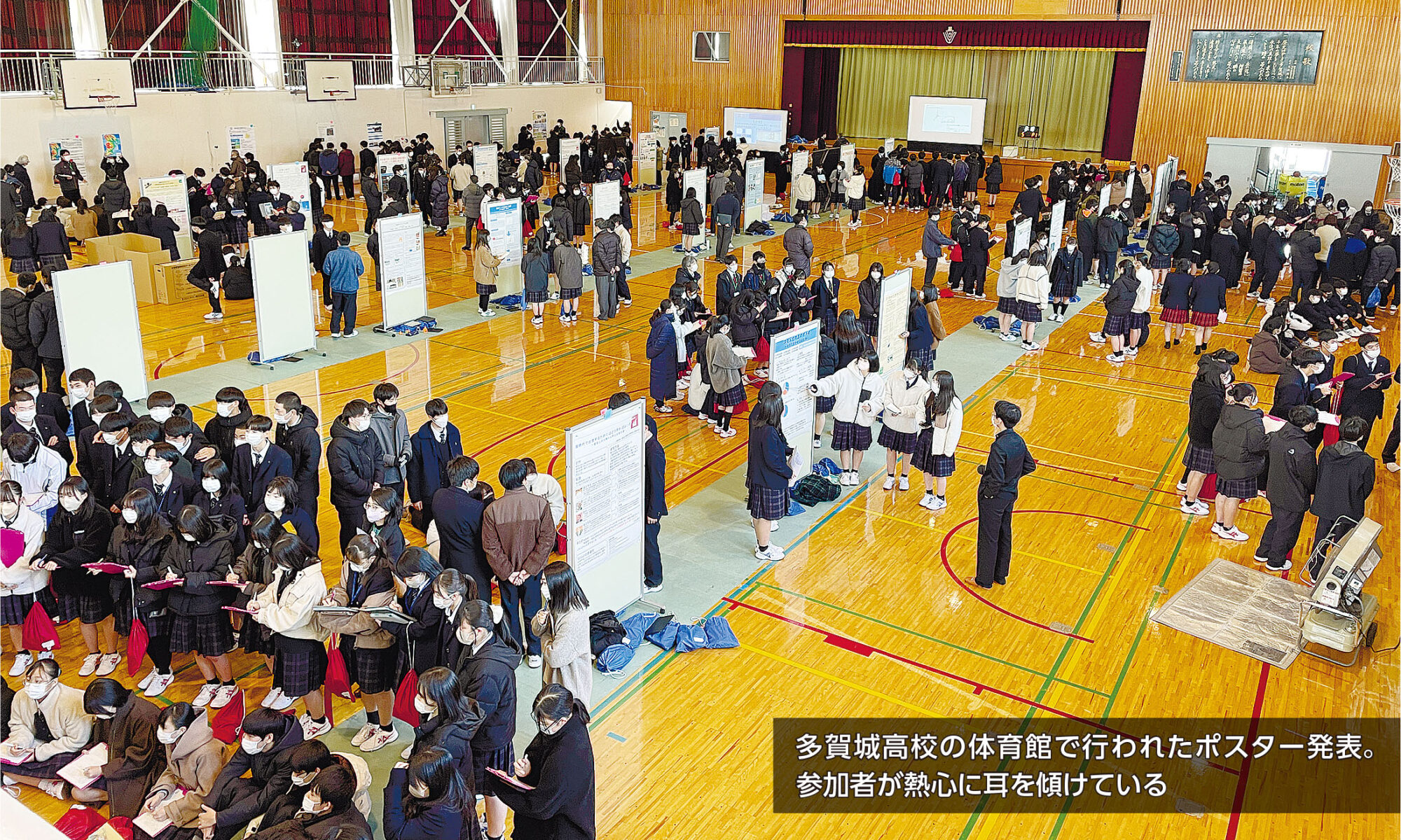 多賀城高校の体育館で行われたポスター発表。参加者が熱心に耳を傾けている